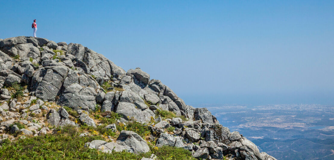 Eine Person auf dem felsigen Gipfel Fóia in der Serra de Monchique in Portugal.