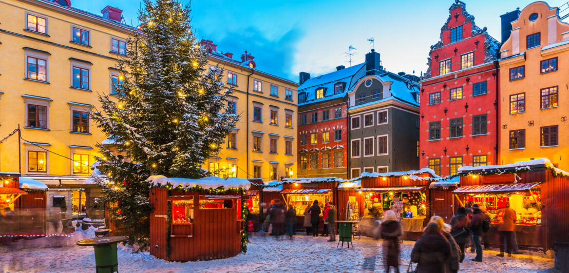 Weihnachtsmarkt auf einem Platz in der Altstadt von Stockholm mit vielen Ständen, Schnee und einem Tannenbaum.