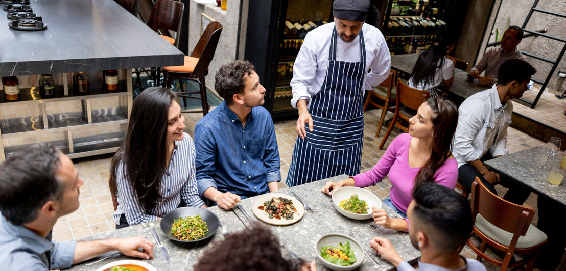 Ein Koch unterhält sich mit einer Gruppe Gäste im Restaurant