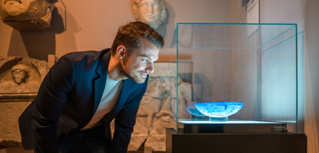 Ein Mann schaut sich eine antike Schale in einer Vitrine in einem Raum mit Skulpturen an.