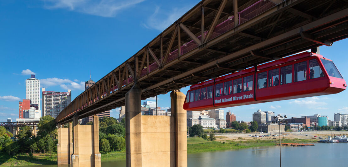 Rote Schwebebahn an einer Brücke über einem Fluss.