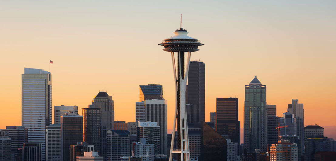 Skyline von Seattle mit Wolkenkratzern und rundem Space-Needle-Turm vor organge gefärbtem Himmel bei Sonnenuntergang.