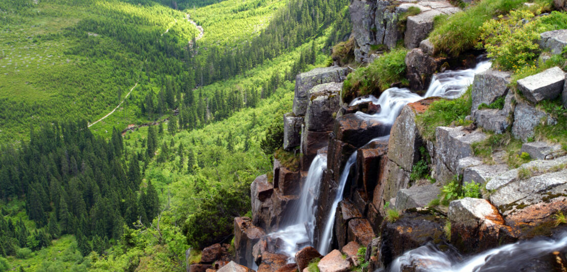 Ein mehrstufiger Wasserfall in einer bewaldeten Berglandschaft.