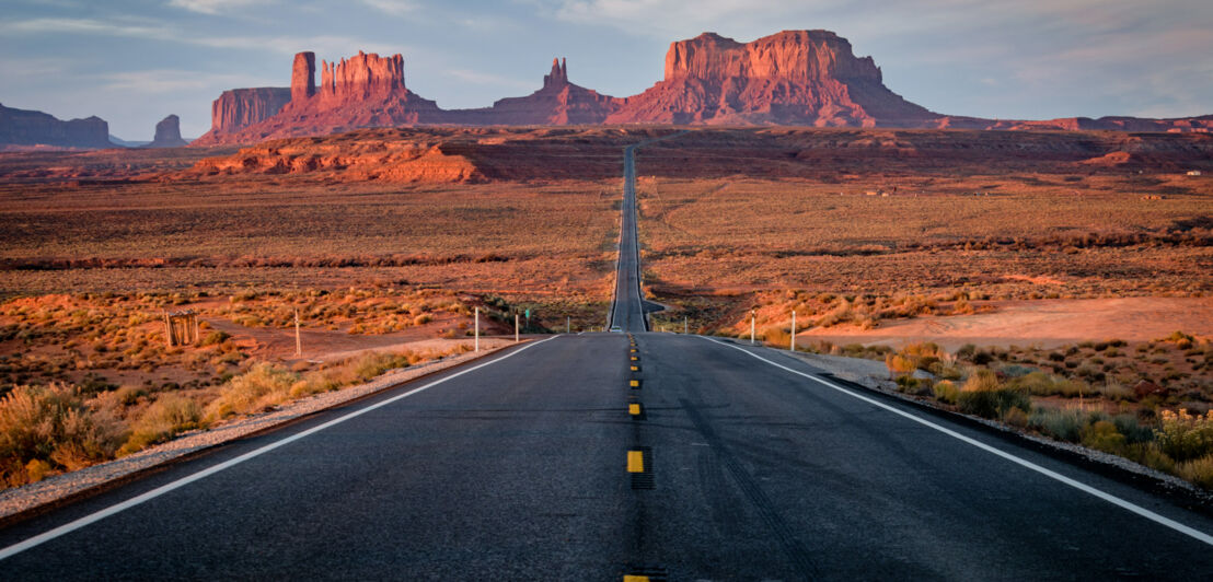 Eine nahezu leere Straße in den USA, die durch eine Landschaft mit rötlichen Steinformationen führt. 