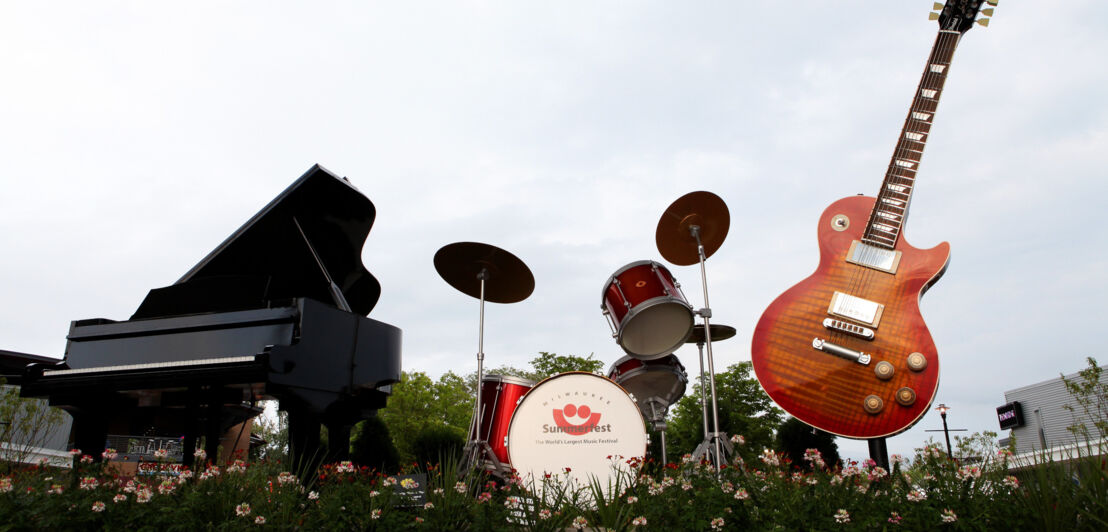 Ein Piano, Schlagzeug und eine E-Gitarre ausgestellt auf einem Blumenbeet im Rahmen des Milwaukee Summerfest Festivals in den USA.