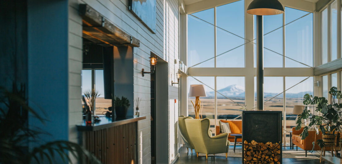 Foyer eines stylishen Hotels mit Holzofen und Blick auf eine weitläufige Landschaft mit schneebedecktem Vulkan.