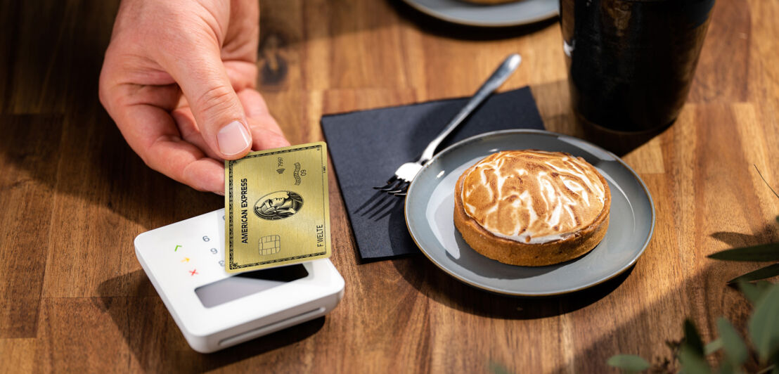 Kontaktlose Zahlung an einem Kartenlesegerät mit einer American Express Gold Card in einem Café. Kontaktlose Zahlung an einem Kartenlesegerät mit einer American Express Gold Card in einem Café.