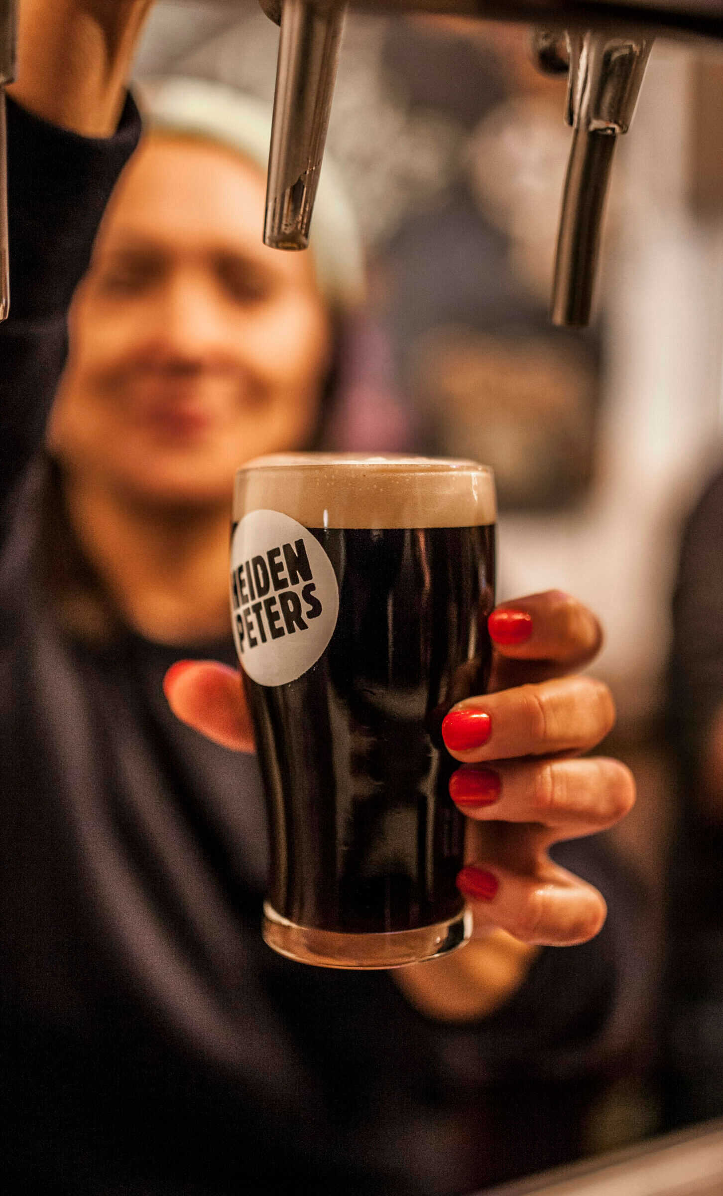 Eine Frau zapft ein dunkles Bier an einem Zapfhahn