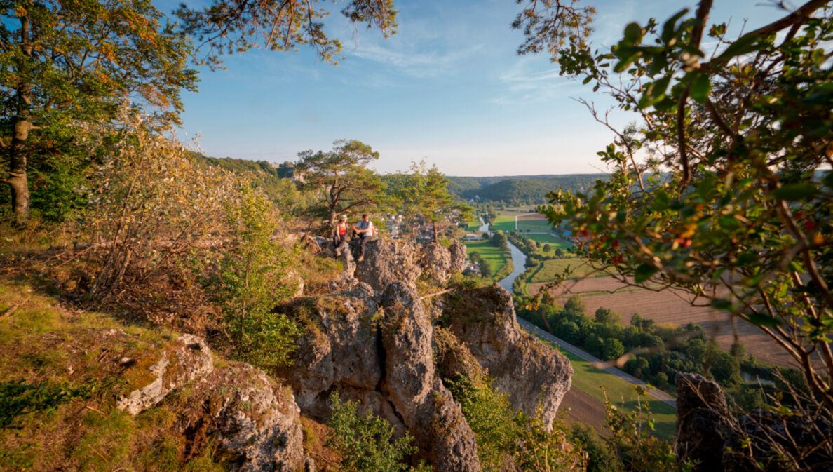 Zwei Wanderer sitzen auf einem Felsen hoch über der Altmühl