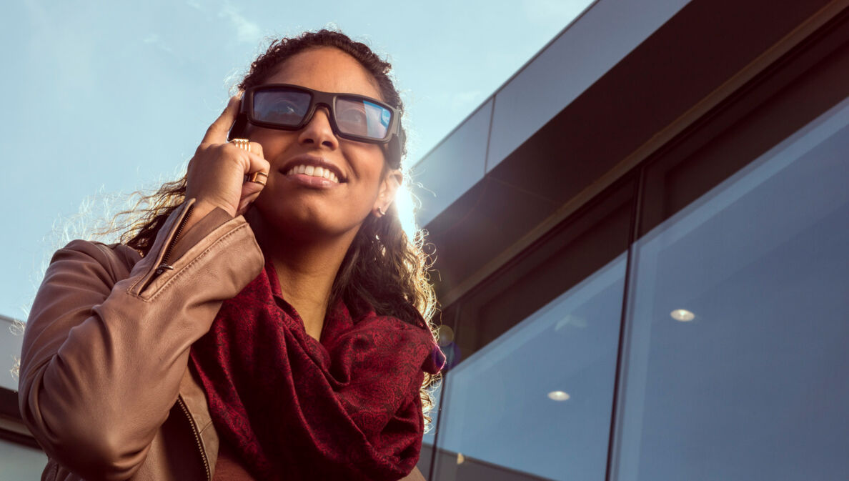 Eine Frau trägt eine Sonnenbrille die sie mit dem Fingern antippt