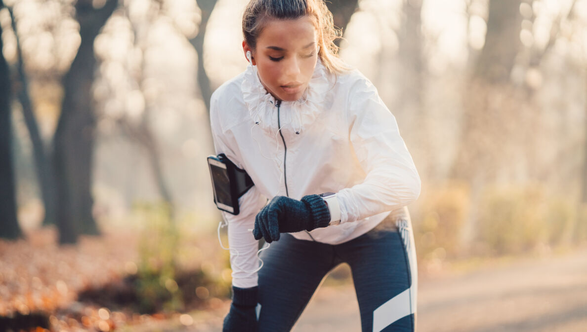 Eine Frau im Joggingdress blickt nach dem Laufen auf ihre Smartwatch