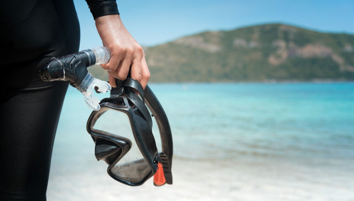 Eine Person am Strand hält eine Taucherbrille und einen Schnorchel