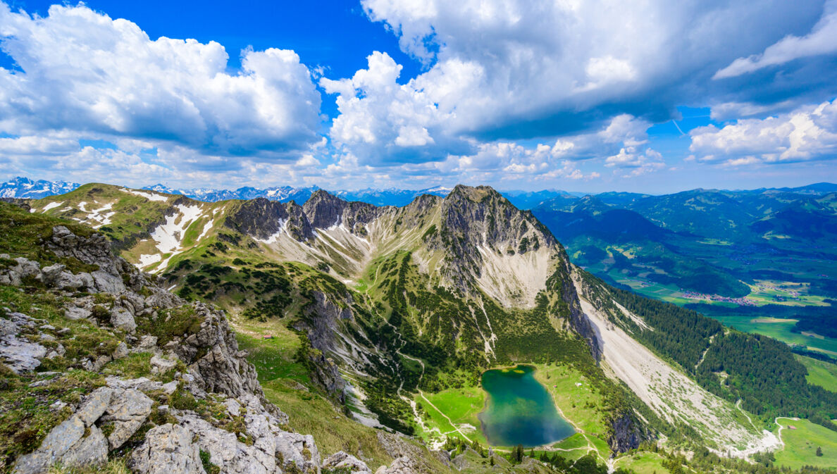 Luftaufnahme eines blaugrünen Bergsees unterhalb eines schroffen Gipfels