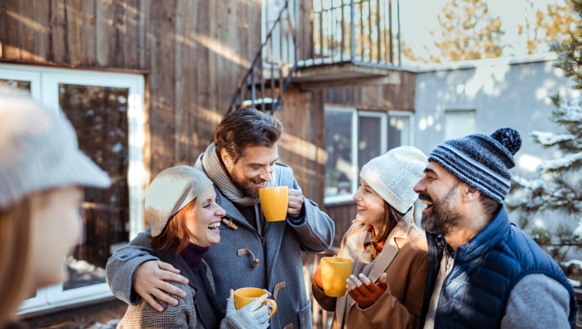 Freunde stehen im Winter vor eine Holzhütte und lachen und reden miteinander