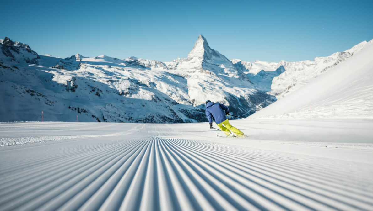 Ein Skifahrer fährt eine perfekt präparierte Piste hinunter, mit Blick auf das Matterhorn