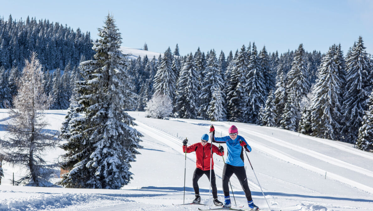 Zwei Skilanglaufende auf Loipe in hügeliger Winterlandschaft