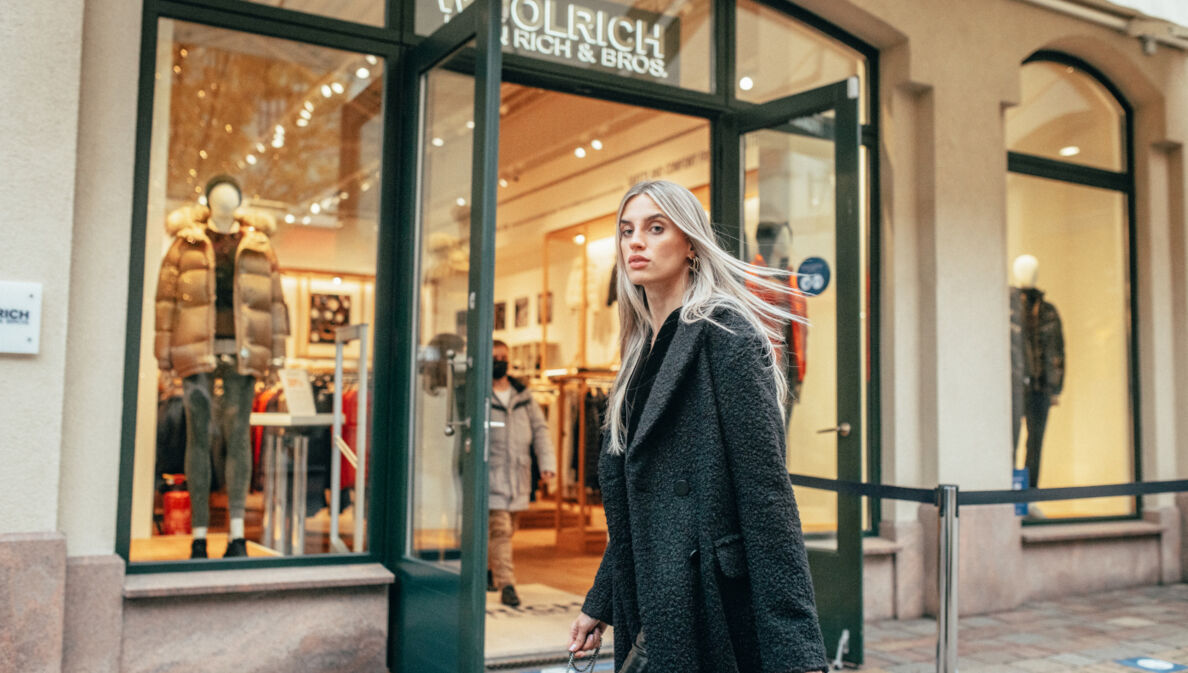 Eine Frau in langem schwarzen Mantel läuft an einem winterlichen Schaufenster vorbei