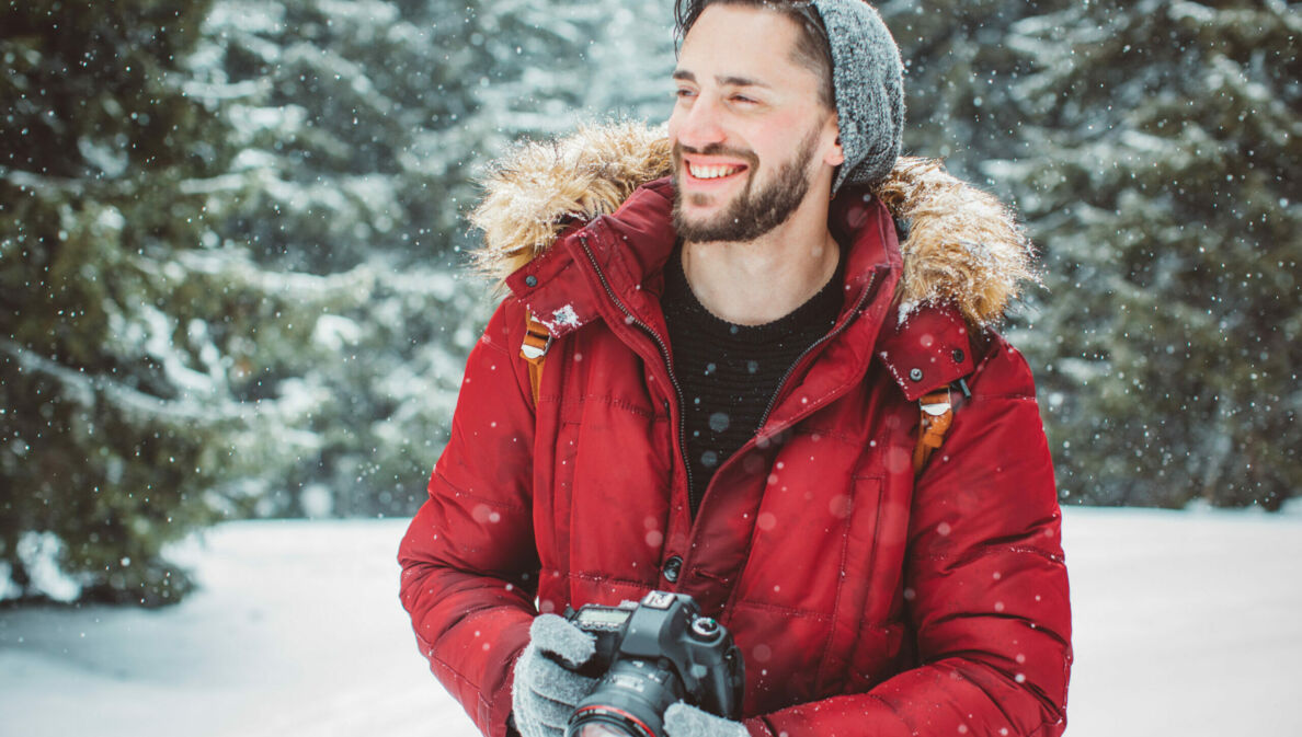 Ein Mann mit Kamera lächelt im Schnee.