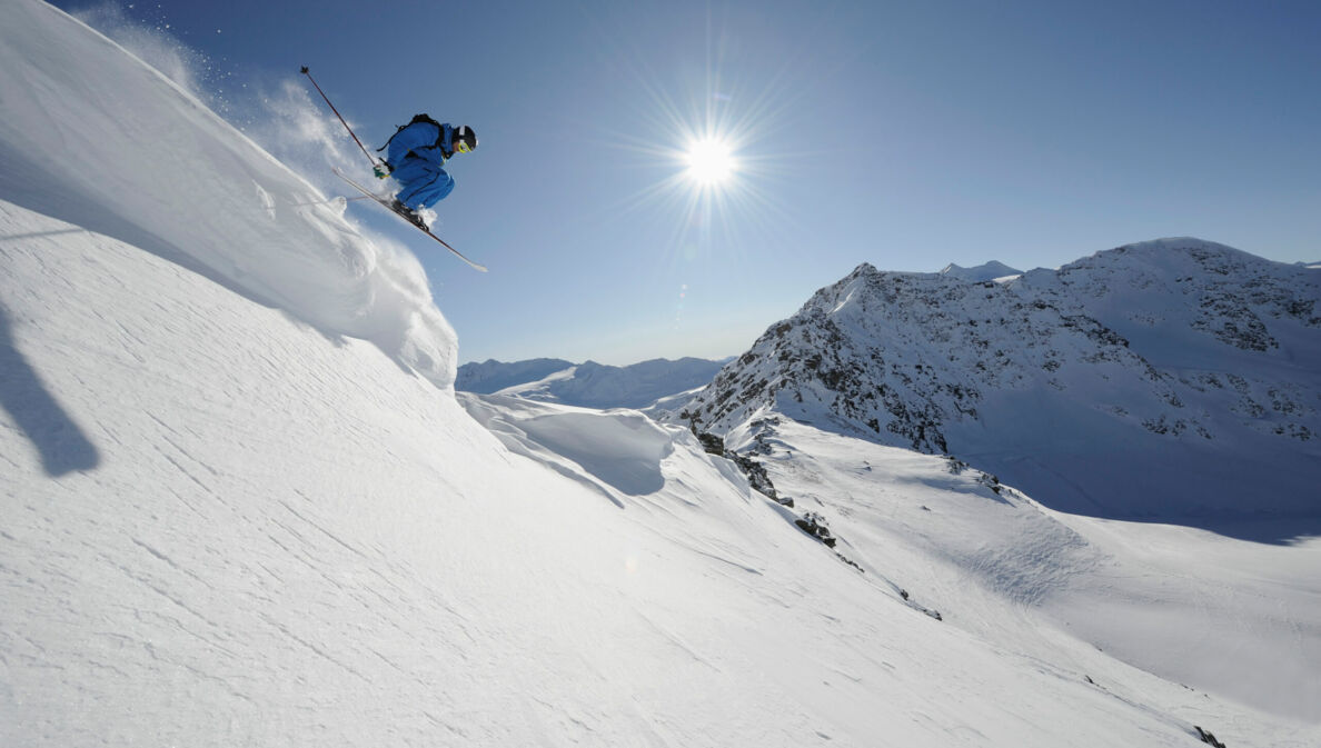 Skifahrer:in springt von einer Klippe, Sonne und Schnee