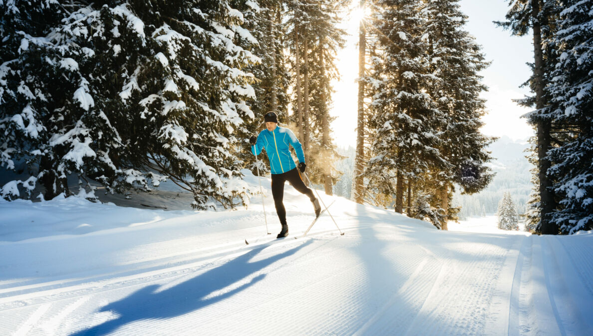 Ein Skilangläufer im klassischen Stil fährt durch den verschneiten Wald