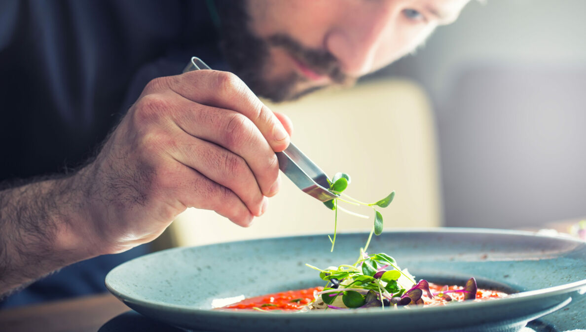 Ein Küchenchef richtet mit der Hand die Tomatensuppe an