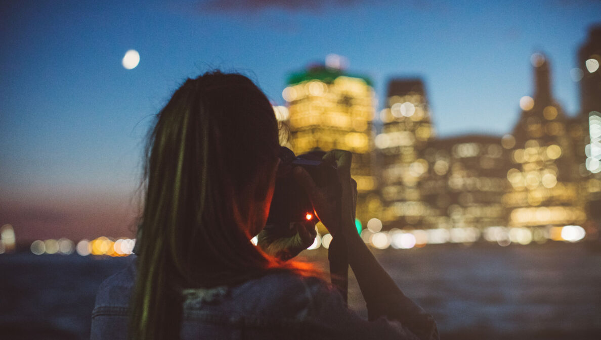 Eine Frau fotografiert in der Dämmerung eine beleuchtete Häuserzeile