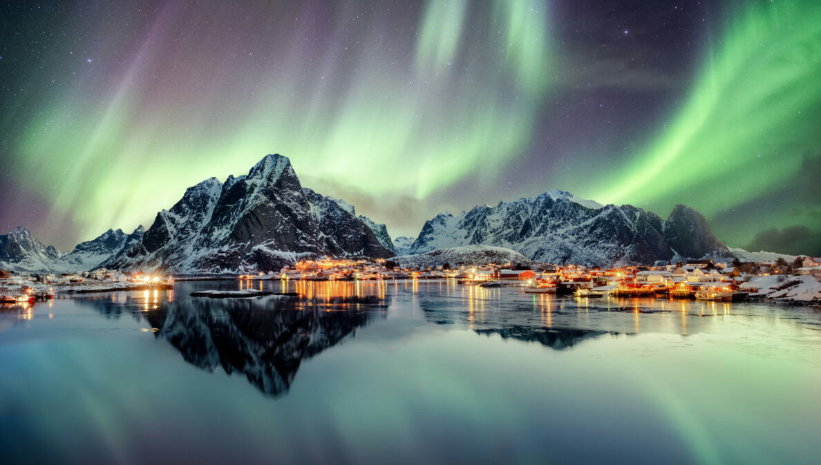 Schneebedeckte Berge und Wasser, darüber grün leuchtende Polarlichter