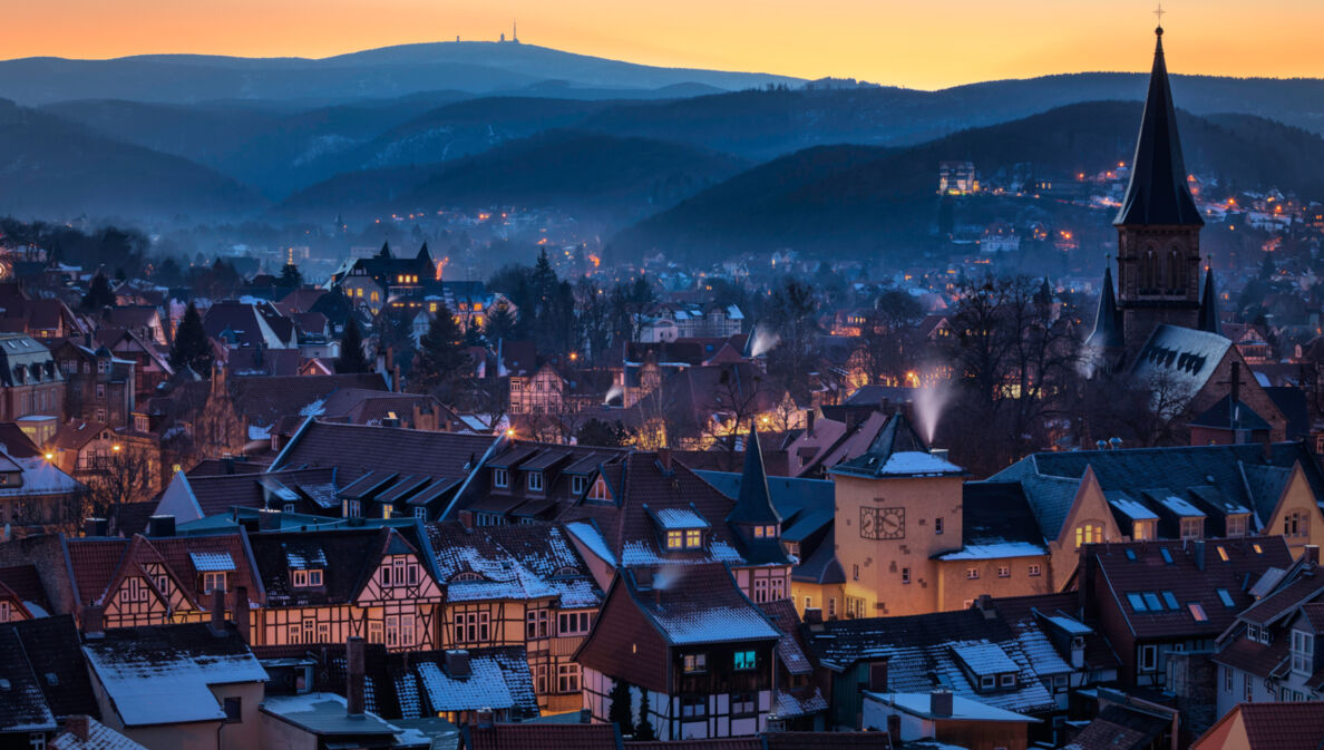 Blick auf eine beleuchtete Fachwerkstadt vor bewaldeten Hügeln