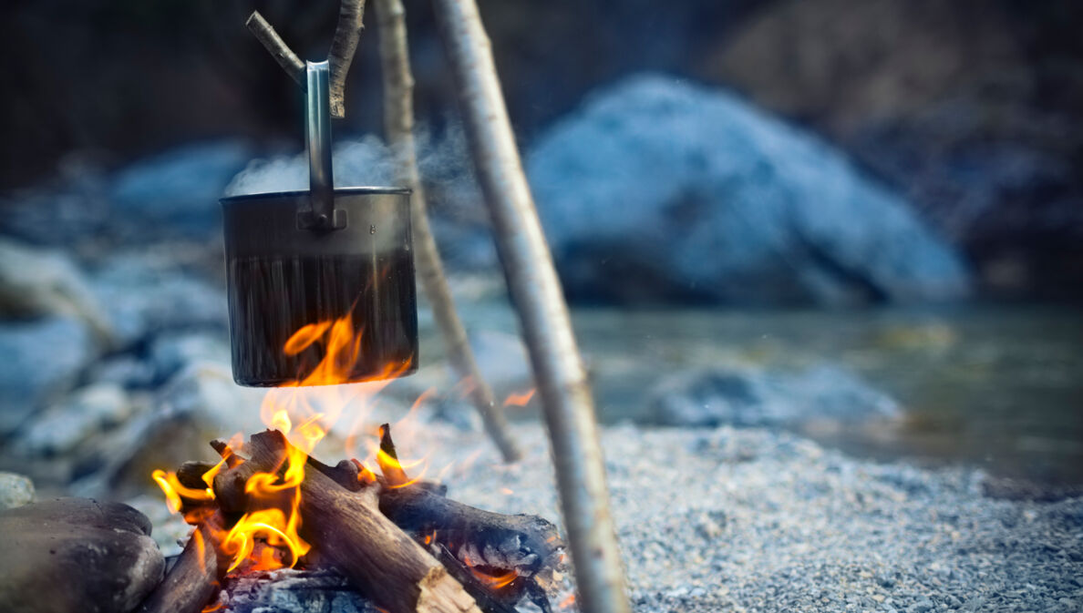 Ein Metalltopf hängt über einer Feuerstelle an einem See in der Dämmerung