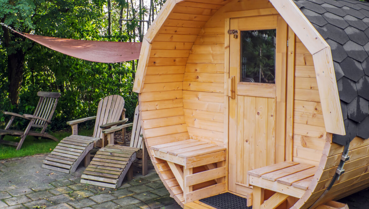 Fasssauna aus Holz im Garten mit Liegestühlen