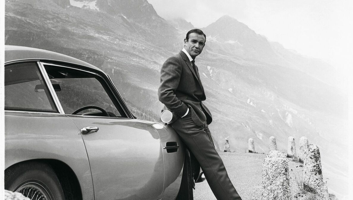 Sean Connery alias James Bond lehnt an einem Aston Martin DB5.