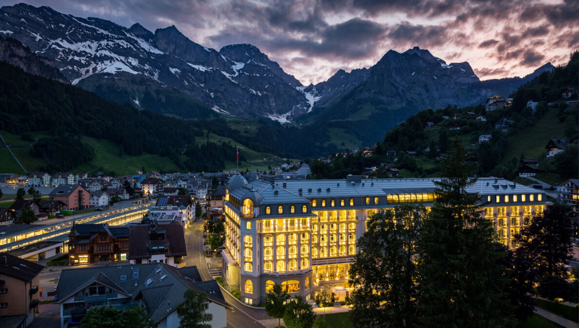 Ein hell erleuchtetes, schlossartiges Gebäude in einem Ort umgeben von Bergen