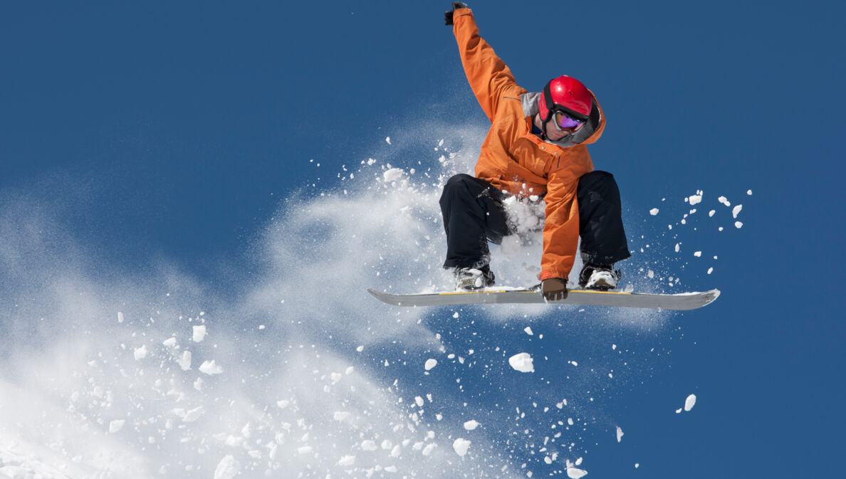 Ein Snowboarder hält sich an dem Board an seinen Füßen bei einem Sprung in der Luft fest