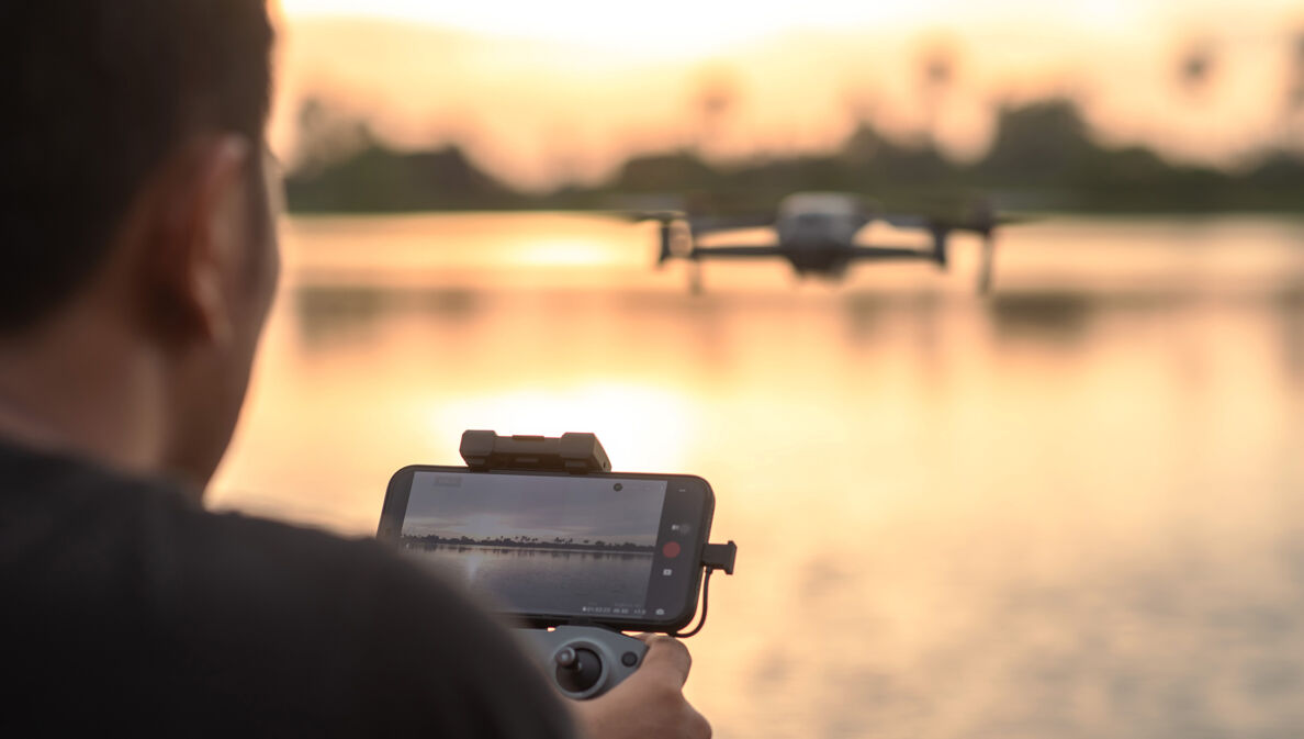 Rückansicht einer Person, die mit einer Drohne per Smartphone einen See fotografiert.