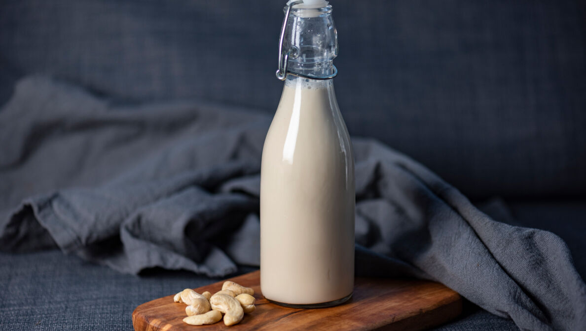 Neben einer Flasche mit Cashewmilch liegen einige Cashewnüsse.