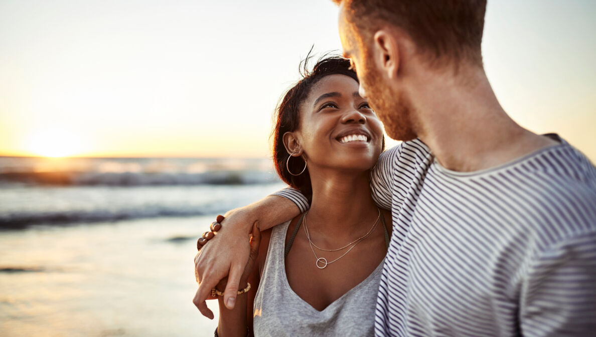 Nahaufnahme eines jungen Paares, das sich glücklich lächelnd am Meer anschaut