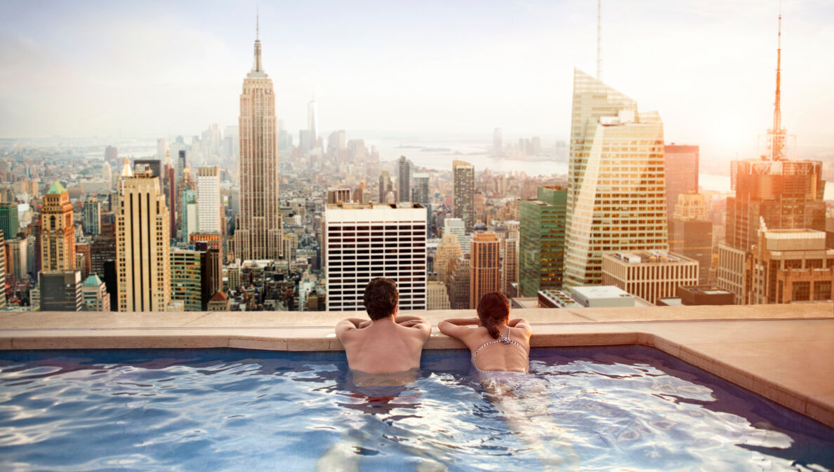 Rückansicht eines Paares in einem Rooftop-Pool, das auf die Skyline von Manhattan blickt