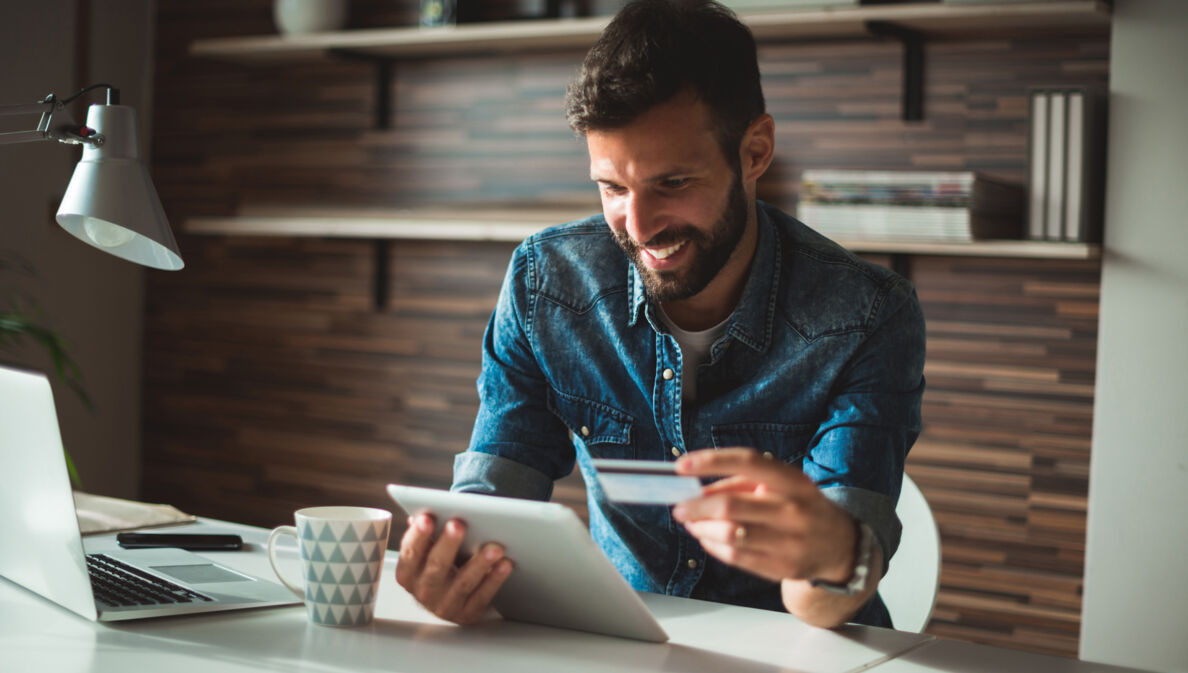 Ein lächelnder Mann am Schreibtisch beim Online-Banking