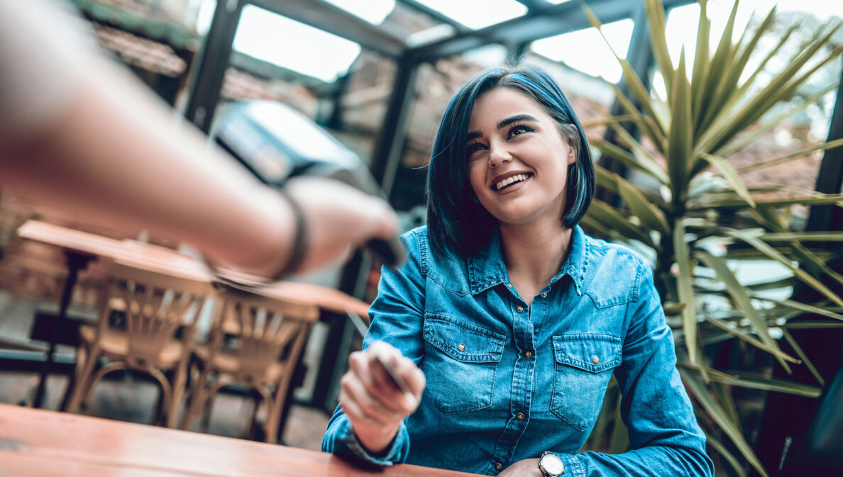 Eine junge Frau zahlt ihren Umsatz im Restaurant per Kreditkarte