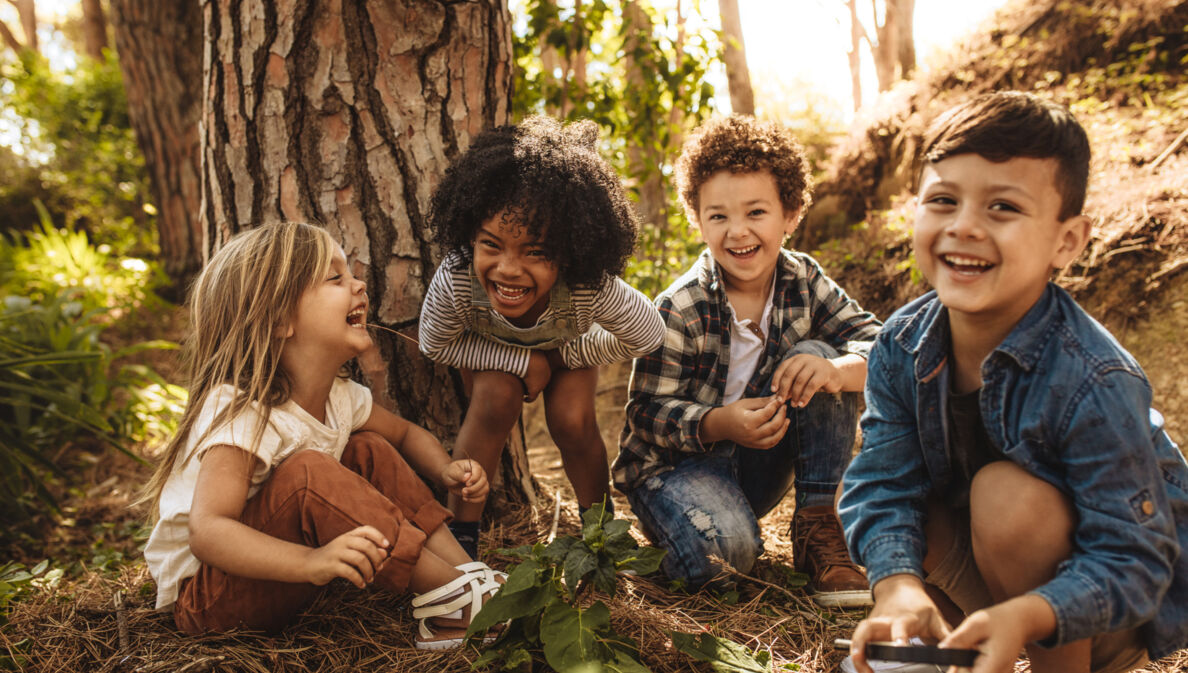 Vier fröhliche Kinder sitzen vor einem Baum im Grünen