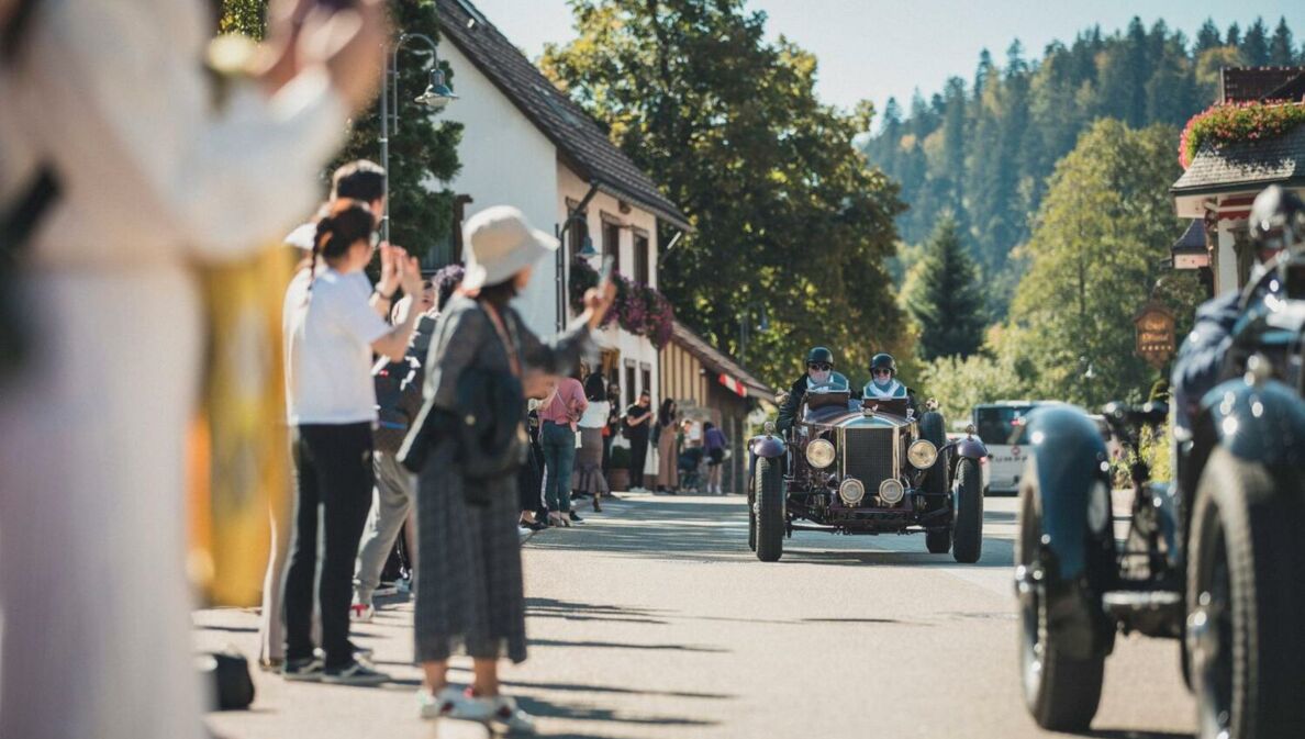 Zuschauer beklatschen Oldtimer auf einer Straße