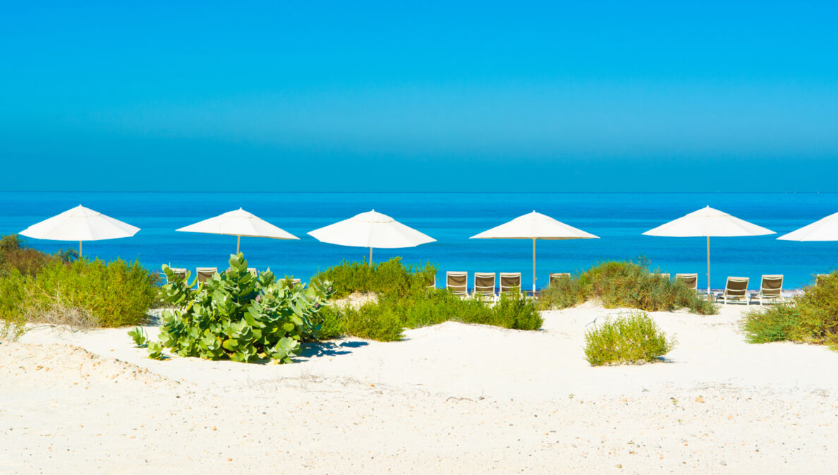 Sandstrand und blaues Meer mit Sonnenliegen und Sonnenschirmen