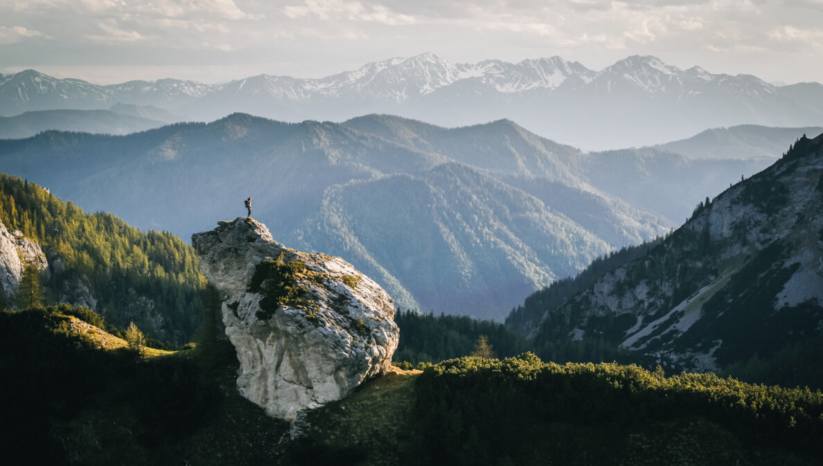 Eine Person beim Wandern auf einem Felsen umgeben von Bergen