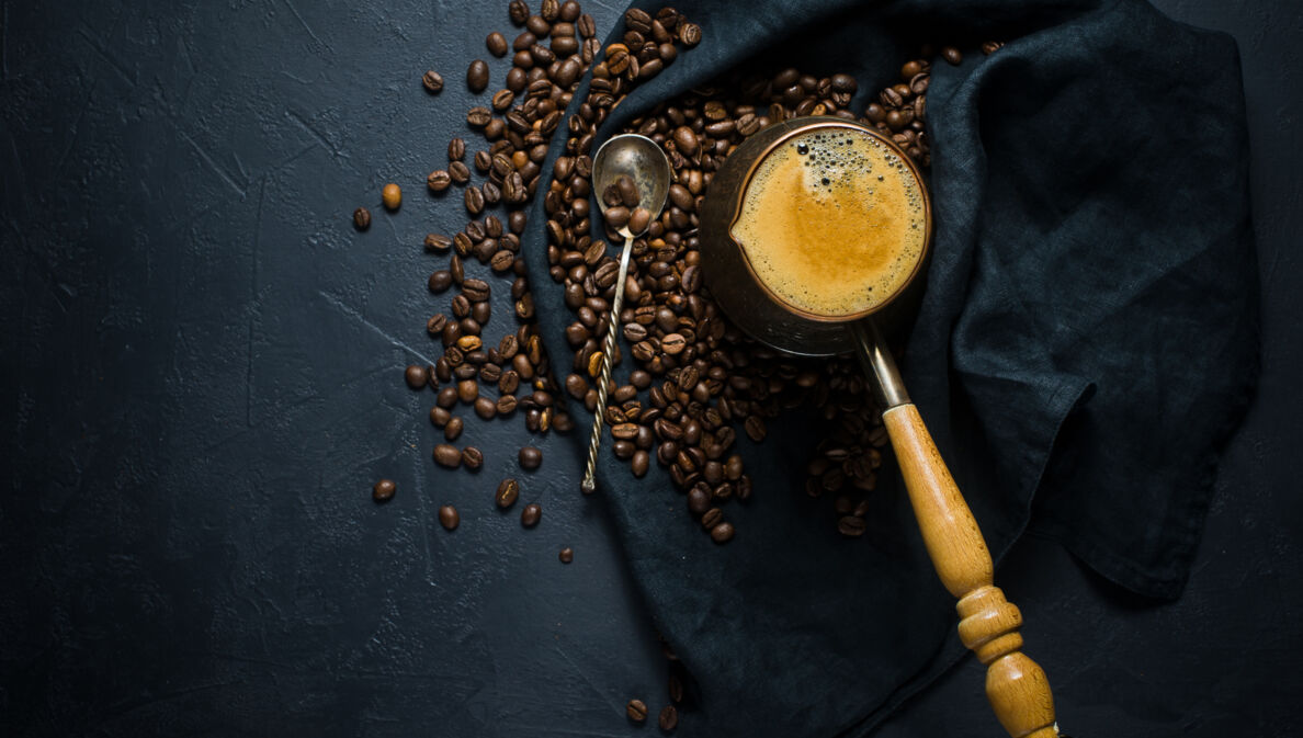 Geröstete Bohnen und frisch gebrühter Kaffee auf einem dunklen Tuch angerichtet