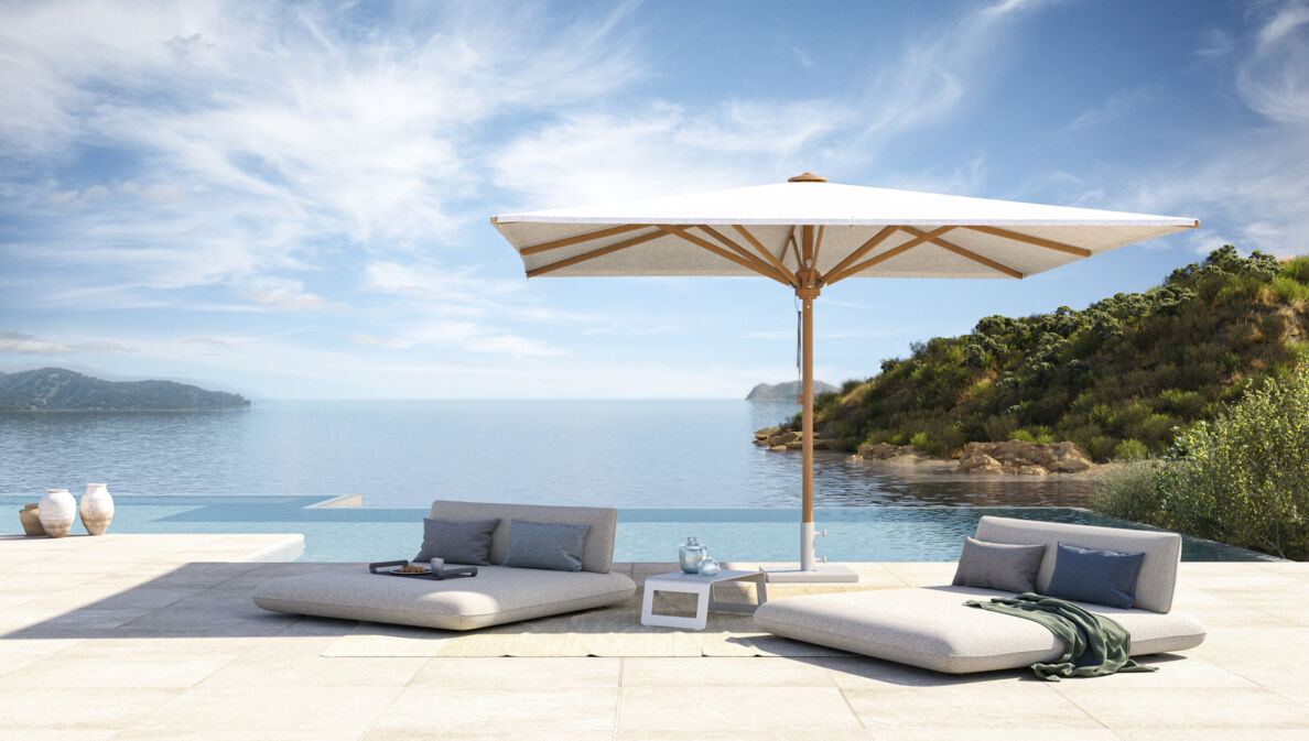 Zwei Gartenbetten und ein Sonnenschirm vor einem Infinitypool, dahinter das Meer