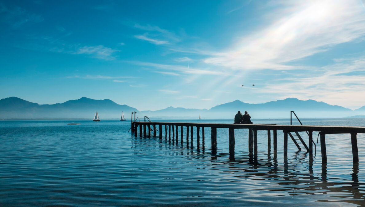 Zwei Personen sitzen auf einem Holzsteg auf dem Chiemsee