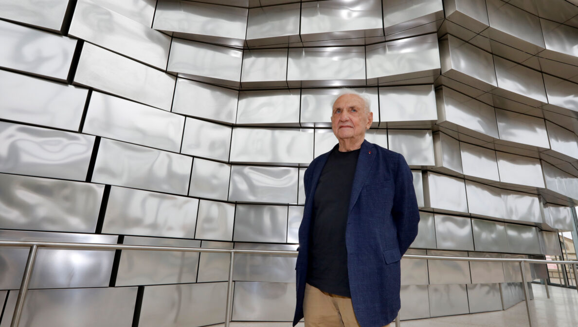 Architekt Frank Gehry vor einer Fassade aus glänzenden Aluminiumplatten