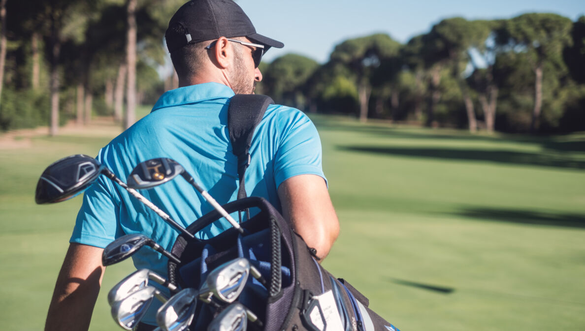 Golfspieler mit Golftasche läuft über einen Golfplatz