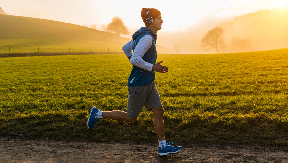 Ein junger Mann joggt im Morgengrauen an einer Wiese entlang