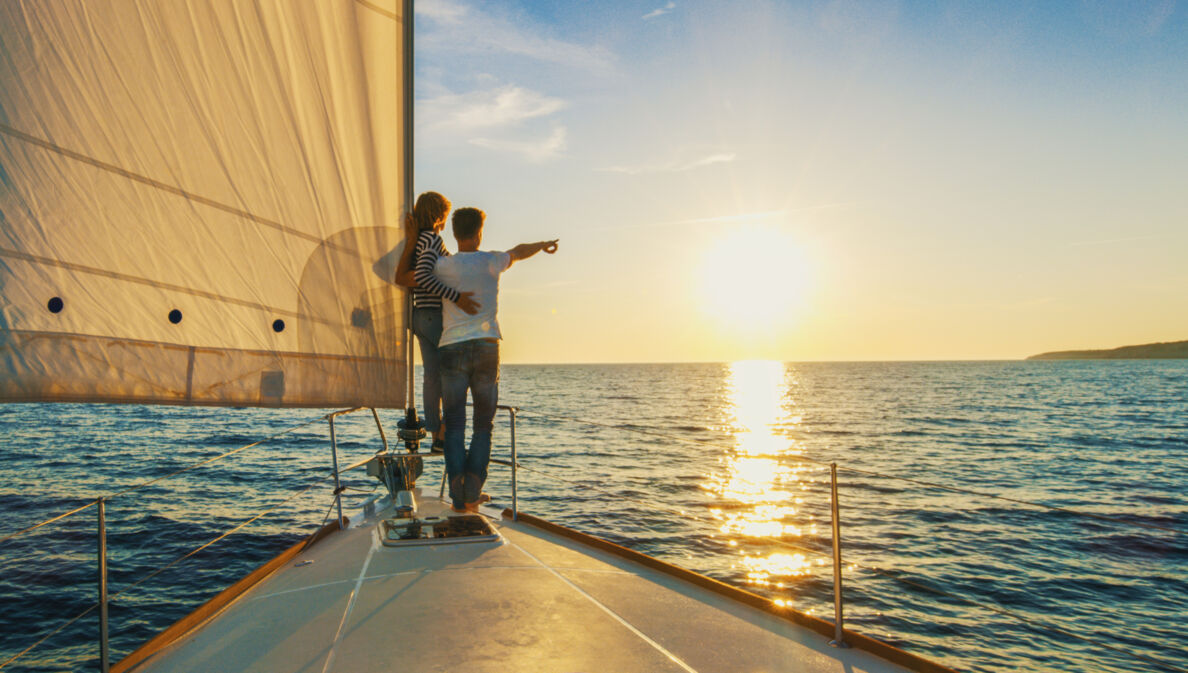 Ein Paar schaut sich auf einem Segelboot den Sonnenuntergang an 